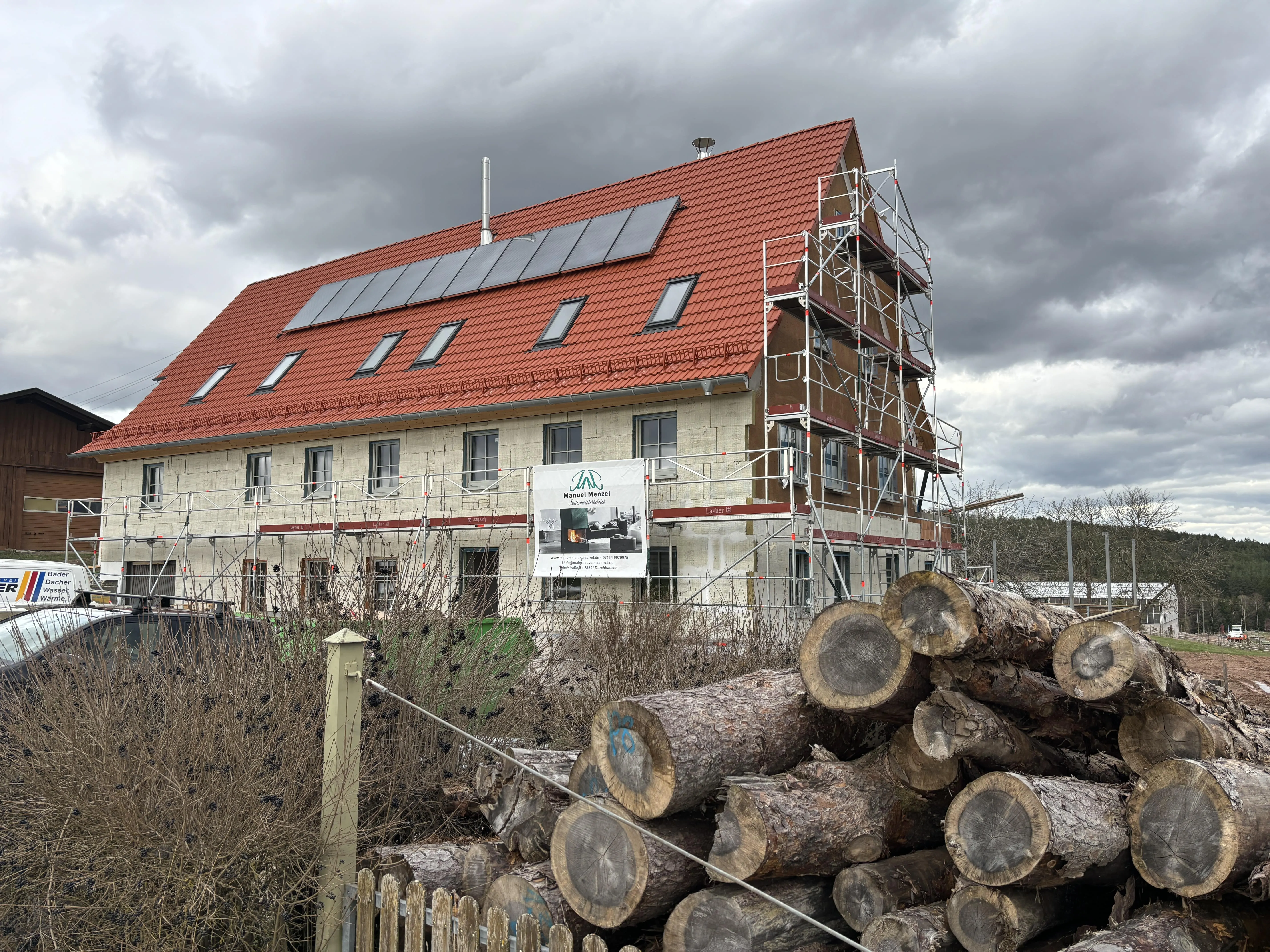 Eingerüstetes Wohnhaus mit Holzstapel im Vordergrund